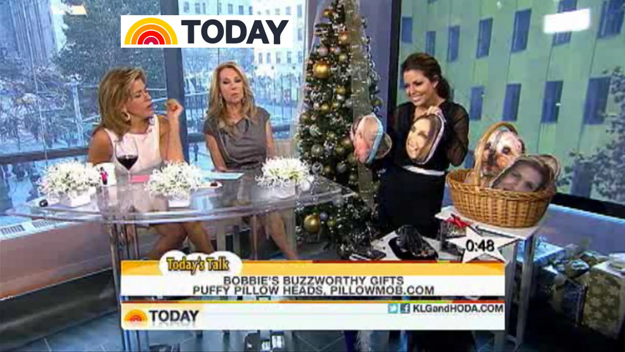 A still from NBC's Today Show. Two hosts sit at a glass desk while a presenter holds up two face pillows beside a basket of more. The caption on screen reads "Bobbie's buzzworthy gifts: puffy pillow heads, PillowMob.com".